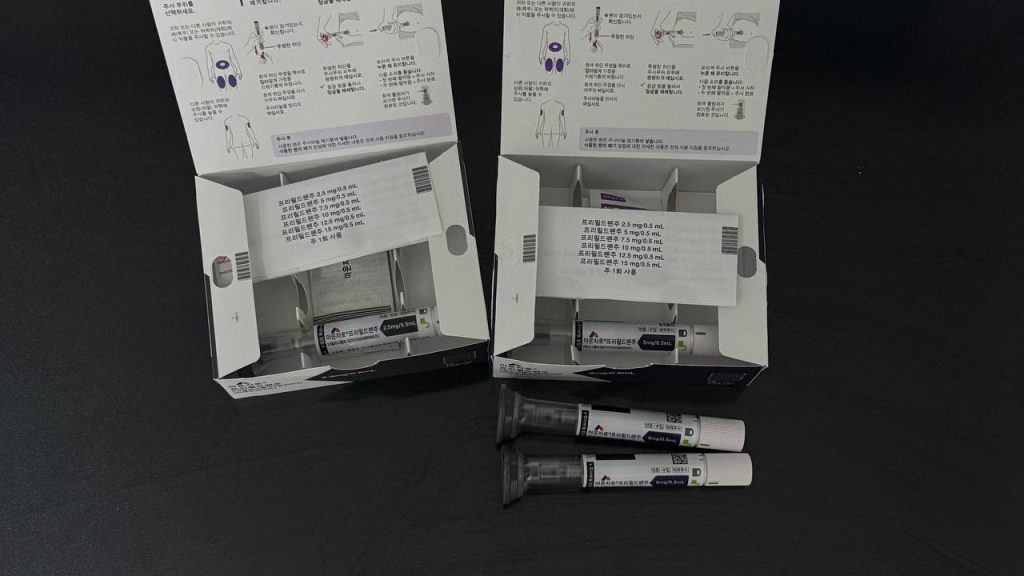 상자가 열려 있는 마운자로 2.5mg 및 5mg 패키지와 나란히 놓인 KwikPen 주사기 실물 사진